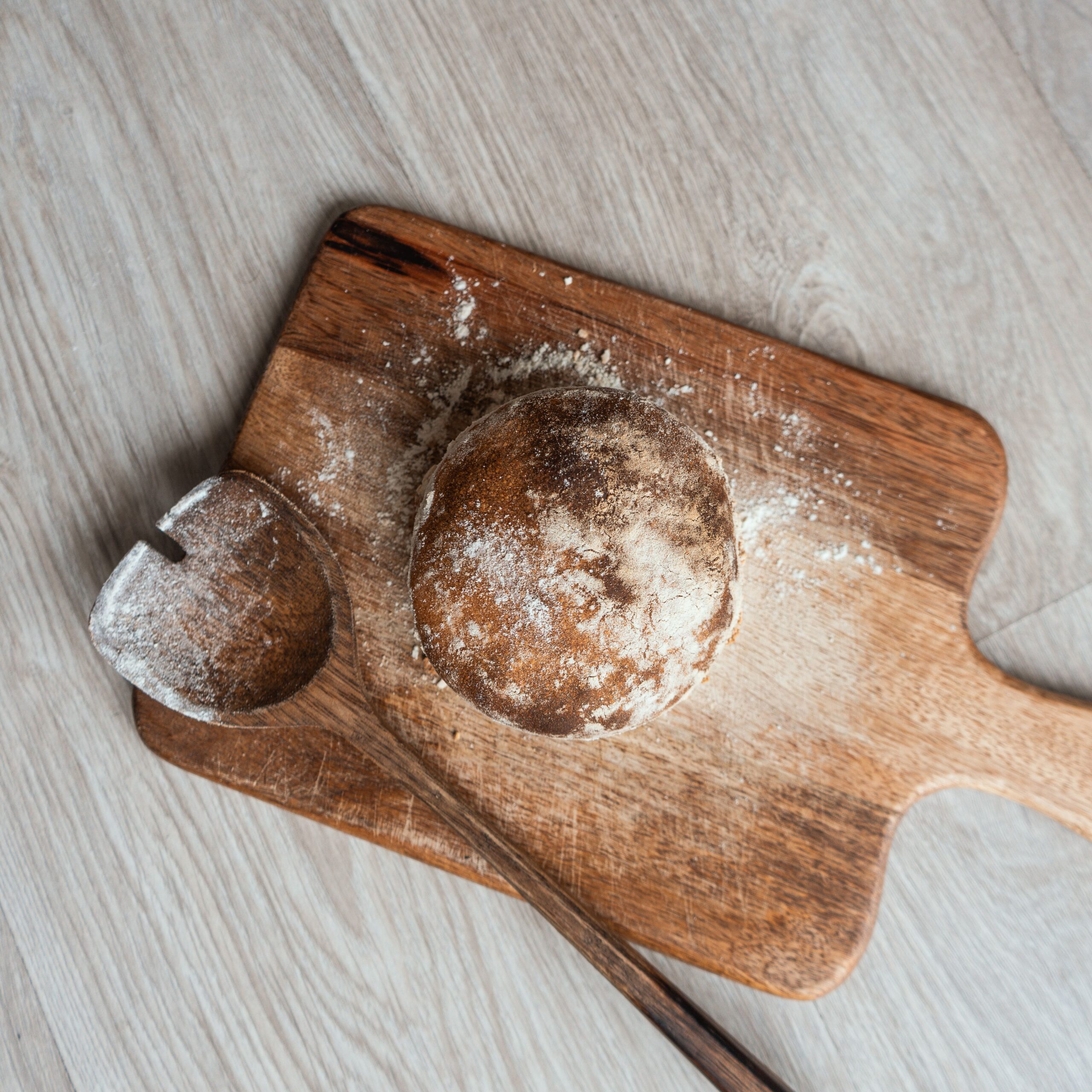 Top view of freshly baked rustic bread on a wooden cutting board with a wooden spoon. Ideal for rustic food photography.